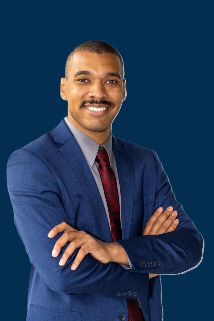 Alexander Taylor in a blue suit with arms crossed, smiling confidently